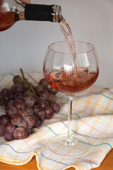 Pouring rosé wine into a glass and a bunch of red grapes.