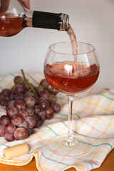 Pouring rosé wine into a glass and a bunch of red grapes.