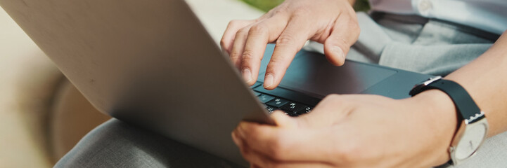 Close-up of hands of young male freelancer typing on laptop keyboard, panorama