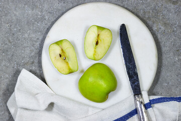 Ripe green half apple with white marble board with napkin on green grunge table. Healthy cooking concept with copy space. Top view