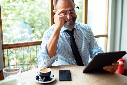 Businessman in a cafe working with tablet and drinking coffee - Powered by Adobe