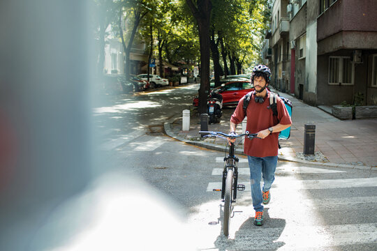 Delivery man with large backpack riding bicycle in urban setting