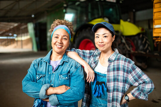 Portrait of two female farmers smiling together in front of farm machinery