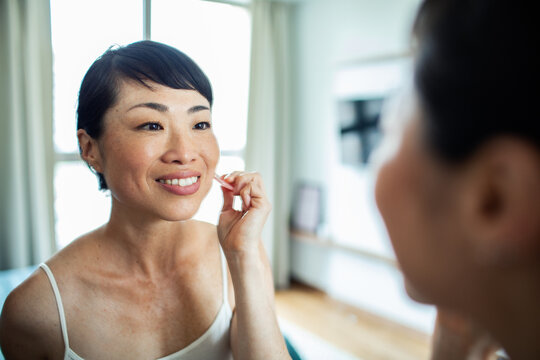 Asian woman checking skin in front of mirror at home