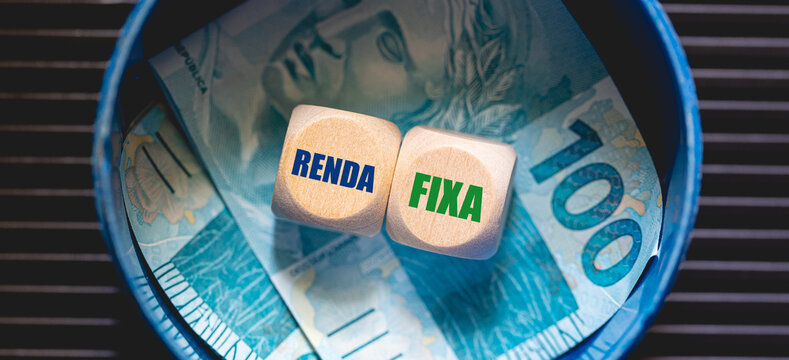 Dois dados de madeira formando o texto renda fixa escrito em Portugu&ecirc;s Brasileiro. Notas de 100 do Real Brasileiro dentro de um cofrinho na composi&ccedil;&atilde;o. Investimento.