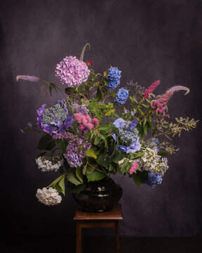 still life with lilac, blue and pink summer flowers in studio in painterly old masters style