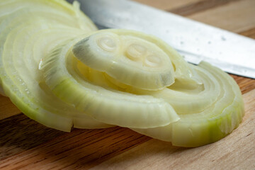 A freshly sliced yellow onion sits on a wooden cutting board with a kniife nearby.