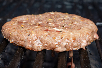 A homemade frozen burger patty is placed on a gas grill.  Patty is partially cooked.  Ready for a flip.