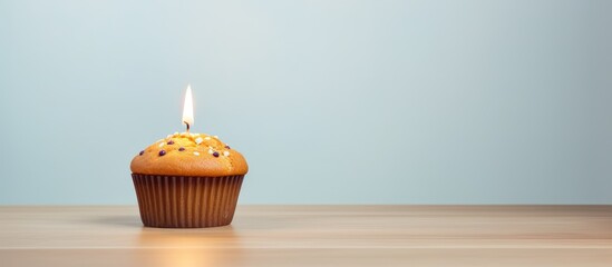 Minimalist copy space image for a birthday celebration with a muffin and burning candle in the background, ideal for an anniversary greeting card.
