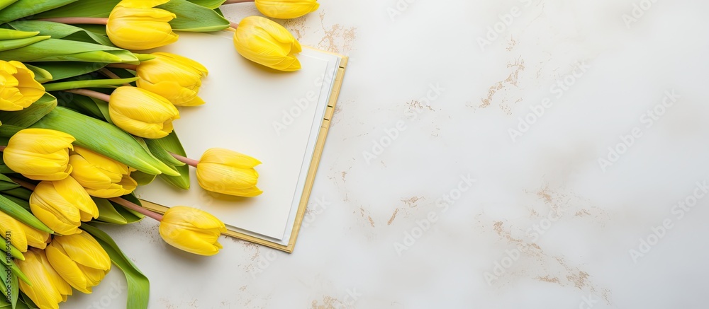 Poster Top view arrangement of fresh yellow tulips on a marble surface with a notepad and sketchbook, providing copy space in a delightful spring-themed image.