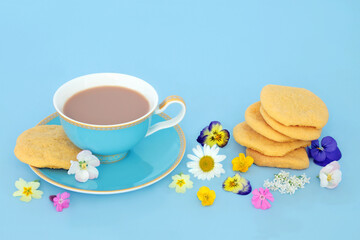Homemade white chocolate chip cookies, teacup and scattered Spring flowers for afternoon tea. Luxury natural floral arrangement for one on blue background.