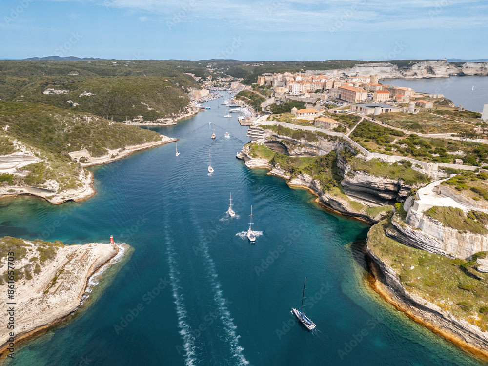 Wall mural Aerial view of sailing boats entering the harbour and passing the walled citadel of Bonifacio in Corsica