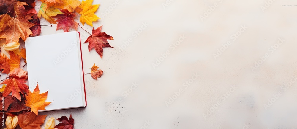 Fototapete An autumn-themed composition featuring a notebook surrounded by colorful autumn leaves against a light background for a captivating copy space image.