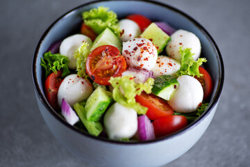 Healthy salad of fresh vegetables and cheese in a plate on a gray background.