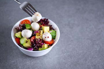 Healthy salad of fresh vegetables and cheese in a plate on a gray background. Fork with cheese.