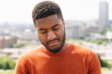 Man With Short Hair Wearing an Orange Sweater Looking Down in Urban Setting