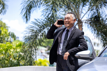 Senior business asian man is talking to the mobile phone by his luxury sedan car for CEO and millionaire manager