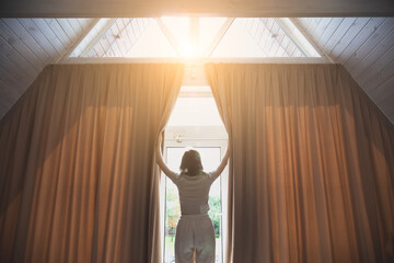 Woman is opening big curtains in modern house.