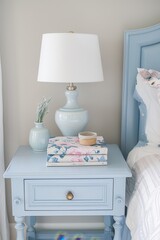Pastel blue nightstand with lamp and a stack of pastel