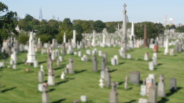 New York City Calvary cemetery in Queens, USA. Manhattan Downtown urban skyline cityscape buildings architecture. Many tombstones on graves, huge graveyard. Large cemetry in United States. Grass lawn.