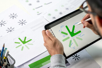 Close-up shot of a graphic designer making notes on logo designs, using a tablet, designing logos,...