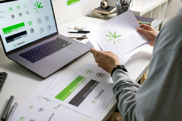 Close-up shot of a graphic designer making notes on logo designs, using tablet and laptop,...