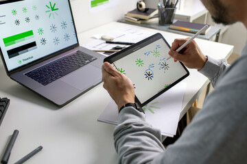 Close-up shot of a graphic designer making notes on logo designs, using tablet and laptop, designing logos, and showcasing the corporate identity and logo design process.