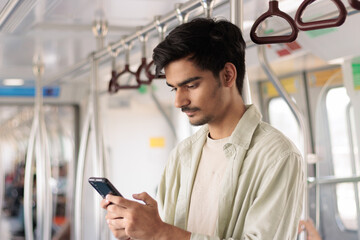 Portrait of young Indian man passenger traveling and using his smartphone in the metro or subway train. Metro and Public transportation concept.