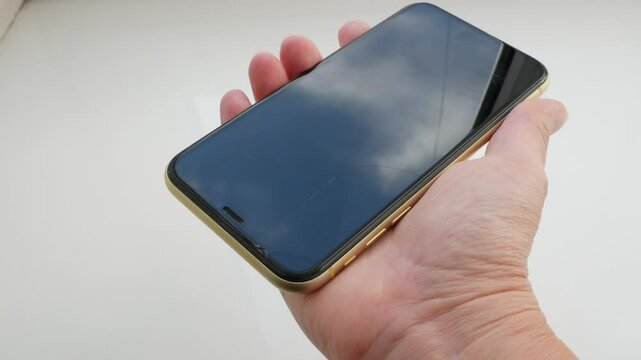 Phone with broken protective glass in hand. Woman hand with shattered cell phone, closeup