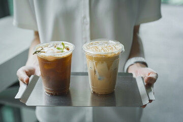 Close up and selective focus hand of employee girl holding tray of ice lychee americano and cappuccino at cafe.