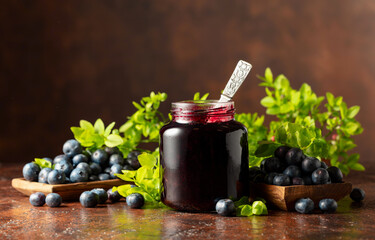 Blueberry jam and fresh berries on a brown background.