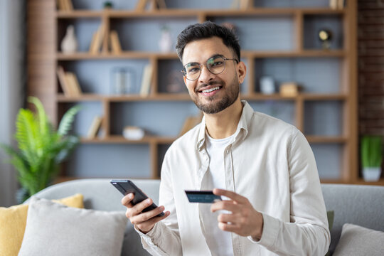 Smiling man holding phone and credit card making online purchase