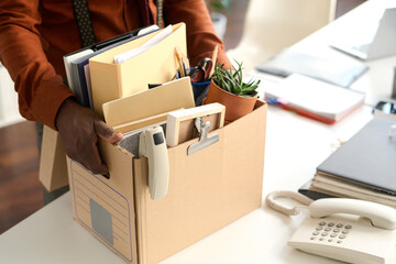 Close up of unrecognizable Black man holding box with personal items in office packing for leave or...