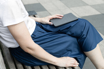 woman reading an e-book sitting on a park bench. man reading an e-book in the park. e-book cover. 