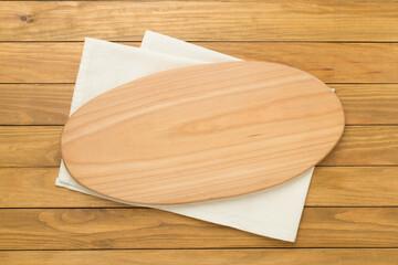Cutting board with napkin on wooden background, top view