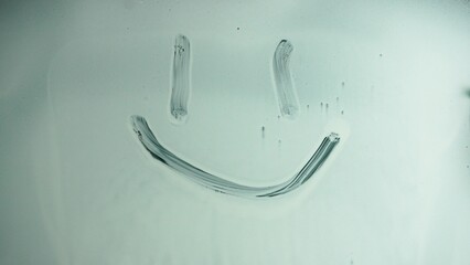 Smiling smiley face painted on glass covered with white liquid paint. Emoji with positive emotion on glass.