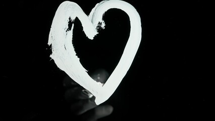 Person using brush with acrylic oil medium white paint and drawing heart sign directly on black glass screen isolated background, opposite view scene.