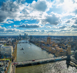 Obraz premium Panoramic aerial drone view of Westminster Abbey, Big Ben, House of Parliament and the River Thames at dusk with the city of London to the horizon under a sunny sky with backlit white clouds.