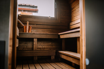 Wooden benches inside a cozy sauna room with a copper bucket and ladle on the upper bench, and a...