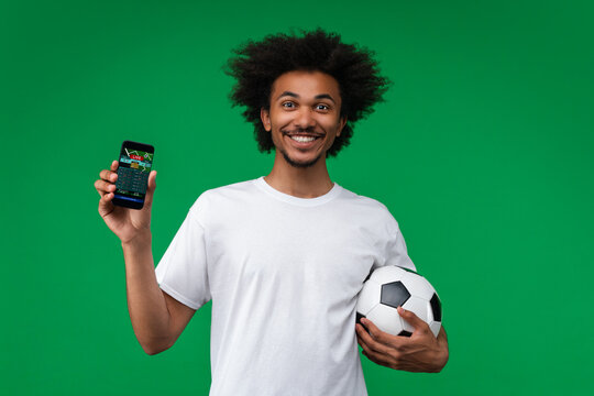 Young happy smiling soccer supporter man showing smartphone with bookmaker's mobile application interface on its screen to the camera