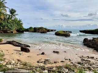 view of a small wild beach with sand and pebbles on a coastline of Guadeloupe in the French West Indies with the Caribbean Sea and rocks in the background
