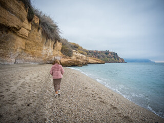 Young woman dressed in a pink coat walking on the beach with a cliff in the background