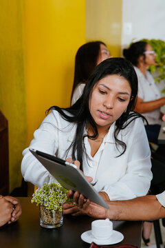 Latin woman discussing business strategies showing data on a tablet during meeting.