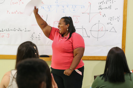 Young plus size Latina student standing in the classroom holding a paper and celebrating.
