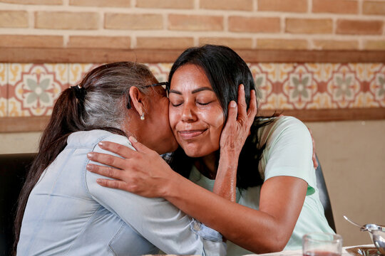 Portrait of a black-haired Latin woman hugging her grandmother affectionately at a family gathering.