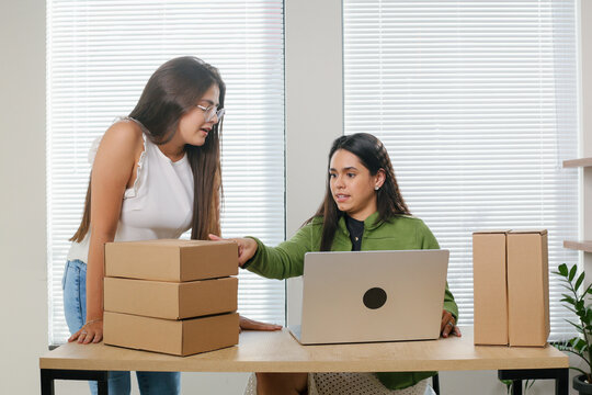 Two women working in e-commerce prepare order box and check online orders for delivery to customer on laptop.