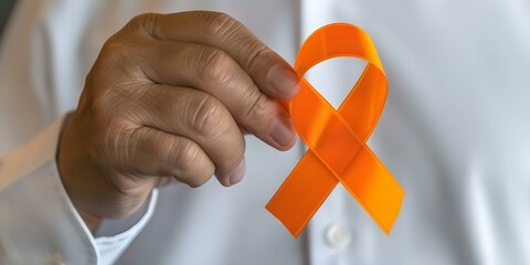 Hand holding orange ribbon symbolizing awareness for leukemia kidney cancer and MS. Concept Leukemia Awareness, Kidney Cancer Awareness, Multiple Sclerosis Awareness, Orange Ribbon, Health Awareness