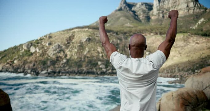 Man, runner and celebration with exercise, back and ocean with fist, excited and progress in workout. Person, winner and hands in air for cheers, success and training goals on run in nature by sea