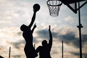 Silhouettes of a basketball player shooting against defender