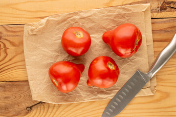 Several red juicy tomatoes with paper bag and knife on wooden table, macro, top view.